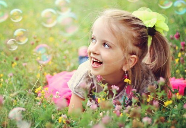 Sweet, happy, smiling six year old girl laying on a grass in a park playing with bubbles and laughing